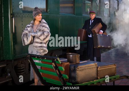 Nachstellungsszene auf dem Bahnsteig in der Nähe eines authentischen 1927 First Class Zugwaggons, wo eine schicke 1920er Dame auf ihr Gepäck wartet Stockfoto