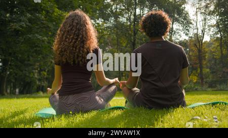 Zurück Ansicht Frau und Mann tun Morgentraining im Stadtpark Natur Grün Gras Fitness Paar sitzen in Lotusstellung Meditieren spirituelle Übungsstunde Stockfoto