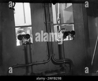 ENTWÄSSERUNG DES ROYAL NAVY-ZUGES AUF DEM MODERNEN SCHULSCHIFF. SEPTEMBER 1941 AN BORD DES ZERSTÖRER-DEPOT-SCHIFFES HMS TYNE. DIE DESTROYERMEN SIND AUSGEBILDET IN GESCHÜTZE, TORPEDOFEUER, U-BOOT-ABWEHR, SEEMANNSCHAFT UND SIGNALGEBUNG. ES WERDEN SCHIFFSMODELLE VERWENDET UND DIE BELEUCHTUNG IST SO ANGEORDNET, DASS SIE DIE EFFEKTE VON SCHEINWERFERN, STERNMUSCHELN UND GESCHÜTZBLITZEN ERZEUGT. - Durch ihre Brille aus kleinen Fenstern hinten in einem verdunkelten Raum beobachten "Kontrollbeamte" den Fall des Schusses. , Stockfoto