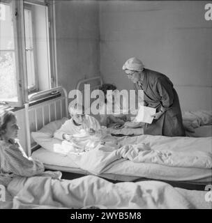 Die britische Sozialarbeiterin Joyce Parkinson vom französischen Hilfsdienst besucht ehemalige Häftlinge in Bergen-Belsen, heute Krankenhauspatienten in Camp Nr. 2, Hohne Military Barracks, April 1945. Stockfoto