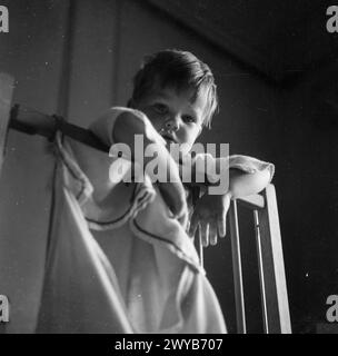 KINDERGARTEN: LIFE AT THE OLD MANOR HOUSE, WENDOVER, BUCKINGHAMSHIRE, ENGLAND, 1944: Ein kleiner Junge lehnt sich über die Gitter seines Kinderbetts, um im Old Manor House, nahe High Wycombe, Buckinghamshire, Gute Nacht zu sagen. , Stockfoto