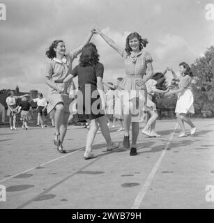 JUGENDVERSAMMLUNG: AUSBILDUNG VON JUGENDORGANISATIONEN, SIDCOT SCHOOL, WINSCOMBE, SOMERSET, ENGLAND, Großbritannien, 1943 - Gruppen junger Frauen halten Hände und springen durch die Bögen, die sie mit ihren Armen machen, während eines Lehrgangs über europäischen Volkstanz an der Sidcot School. Die Klasse ist Teil des körperlichen Trainings, das Teil des einwöchigen Jugendtrainings ist. , Stockfoto