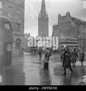 COVENTRY, FRÜHJAHR 1944: ALLTAGSLEBEN IN COVENTRY, WARWICKSHIRE, ENGLAND, Großbritannien, 1944 – Fußgänger und Busse beeilen sich, wenn sie ihre täglichen Geschäfte auf der High Street, Coventry, erledigen. Der Fokus dieses Fotos ist die Kathedrale, deren Turm hinter einigen Postern des Informationsministeriums zu sehen ist. , Stockfoto