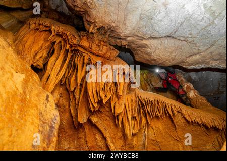 Ein Speläologe mit Helm und Scheinwerfer, der eine Höhle mit reichen Stalaktiten- und Stalagmitenformationen erforscht. Hochwertige Fotografie. Stockfoto