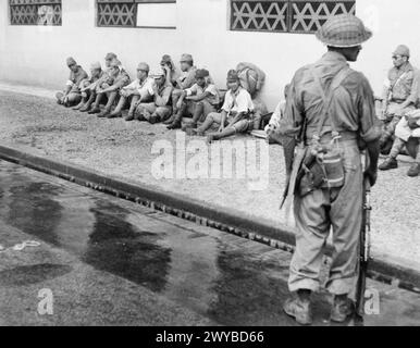 BRITISCHE WIEDERBESETZUNG SINGAPURS, 1945 - Ein Soldat der 5. Indischen Division wacht über japanische Gefangene vor ihrem ehemaligen Hauptquartier in Singapur. , Stockfoto