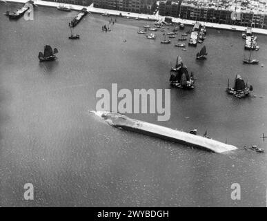 BEFREIUNG HONGKONGS. 30. AUGUST 1945 UND DANACH. SZENEN NACH DER WIEDERBESETZUNG DER KRONENKOLONIE. - Bombardiert und gestrafft, bis es sank, und auf seiner Seite zur Ruhe kam, war dieses Wrack eines von vielen, die gefunden wurden, um Victoria Harbour in Hongkong zu behindern. Auch chinesische Dschunks sind zu sehen, von denen sich viele um die Kriegsschiffe versammelten, als sie ankerten. , Stockfoto