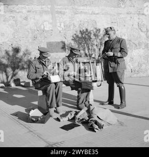 Kriegsberichterstatter schreiben auf dem Hauptplatz von Tripolis, wie ein italienischer Polizeibeamter während des Eintritts der Achten Armee beobachtet. Stockfoto