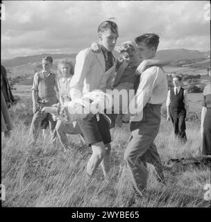 KOOPERATIVE JUGENDSOMMERSCHULEN: BILDUNG UND UNTERHALTUNG, CRAIG SCHOOL, WINDERMERE, ENGLAND, VEREINIGTES KÖNIGREICH, JULI-AUGUST 1943: Eine Gruppe junger Menschen, die die Co-operative Union Summer School an der Craig School am Lake Windermere besuchen, üben erste Hilfe bei einem Spaziergang auf den Fjells. Zwei Jungen tragen ein Mädchen, das ihre Beine zusammengebunden hat, wobei einer als Schiene für das andere, gebrochenes Bein benutzt wird. Die erste-Hilfe-Kurse an der Summer School in Windermere wurden von Herrn F Kay von der St. John's Ambulance Brigade geleitet. , Stockfoto