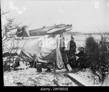 BOMBERKOMMANDO DER ROYAL AIR FORCE, 1942-1945. - Die Bodencrew wärmt sich auf einem Ofen im Schnee in Rufforth, Yorkshire, bevor sie sich auf die Dispersion hinter ihnen aufmacht, um ein Handley Page Halifax der Heavy Conversion Unit Nr. 1663 zu bedienen. Royal Air Force, Heavy Conversion Unit, 1663 Stockfoto