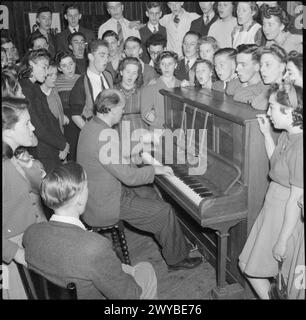 KOOPERATIVE JUGENDSOMMERSCHULEN: BILDUNG UND UNTERHALTUNG, CRAIG SCHOOL, WINDERMERE, ENGLAND, VEREINIGTES KÖNIGREICH, 1943: Junge Menschen, die die Co-operative Union Summer School besuchen, stehen am Klavier und werden von einem Musiklehrer gespielt (wahrscheinlich Herr Dawn von der St George's Co-Educational School in Harpenden) und singen. Sie haben eine „offizielle“ Musikgruppe und einen Chor in der Schule, mit stundenlangem Üben, aber der Lehrer spielt auch Klavier für ein allgemeineres Abendlied. Der Originaltitel besagt, dass englische, schottische und walisische Lieder sehr beliebt waren und manchmal auch eine Gruppe walisischer Mädchen Stockfoto