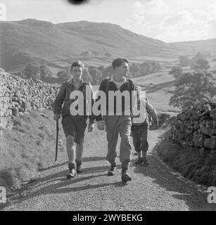 JUNGE WANDERER IN YORKSHIRE: DIE ARBEIT DER YOUTH HOSTEL ASSOCIATION IN WARTIME, MALHAM, YORKSHIRE, ENGLAND, VEREINIGTES KÖNIGREICH, 1944: Eine Gruppe junger Männer spaziert auf einer sonnigen Straße in Yorkshire. Sie sind vom Jugendherberge in Malham aus aufgebrochen. Hinter ihnen kann man einen beeindruckenden Blick auf die Hügel und die Landschaft genießen. , Stockfoto