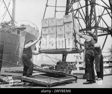 GROSSBRITANNIEN LIEFERT DIE GÜTER IN KRIEGSZEITEN: HAFENARBEITER IN BRISTOL, ENGLAND, 1940 - Güterkisten werden mit einem Brückenkran auf einen wartenden Dampfer an einem Bristol-Dock geladen. Jeder der Kisten ist mit einer Unionsflagge und dem Aufdruck "Britain Delivers the Goods" versehen. , Stockfoto