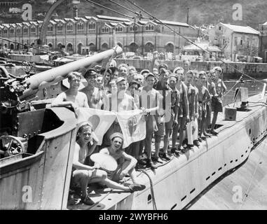 BEFREIUNG HONGKONGS. 30. AUGUST 1945 UND DANACH. SZENEN NACH DER WIEDERBESETZUNG DER KRONENKOLONIE. - Männer von HM U-Boot SPEERSPITZE mit drei Ex-Kriegsgefangenen in ihrer Mitte, die stolz Gefangene japanische Flaggen zeigen, nach der Wiederbesetzung Hongkongs. Die HMS SPEERHEAD war eines von acht U-Booten, die Teil der britischen Task Force waren, die am 30. August in den Hafen eindrang. , Stockfoto