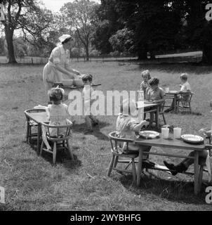 KINDERGARTEN: LEBEN IM ALTEN HERRENHAUS, WENDOVER, BUCKINGHAMSHIRE, ENGLAND, 1944 - Eine Krankenschwester serviert Mittagessen für Kinder, die an Tischen und Stühlen sitzen, die auf dem Gras im sonnigen Garten des Kindergartens im alten Herrenhaus in Wendover liegen. Der Originaltitel besagt, dass die Kindermahlzeiten, wann immer möglich, im Freien serviert werden. , Stockfoto