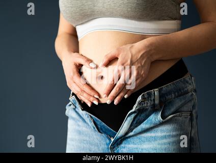 Magen der Schwangeren, erstes oder zweites Trimenon. Frühschwangerschaft. Gesunde Bauch- oder Bauchschmerzen. Herz mit Händen. Menstruationsschmerzen, Gynäkologie. Stockfoto