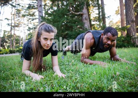 Ein Mann und eine Frau machen Liegestütze auf einem grasbewachsenen Feld. Die Frau ist auf den Knien und der Mann auf Händen und Knien Stockfoto