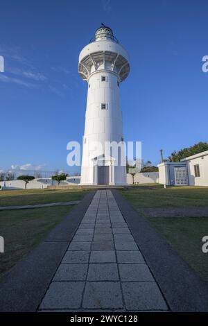 Ein majestätischer weißer Leuchtturm steht hoch unter einem klaren blauen Himmel mit einem Pfad, der zu ihm führt Stockfoto