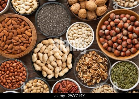 Erdnuss, Haselnuss, Walnuss, Mandeln, Pistazien, Sonnenblumen, Kürbis, Chia, Pekannuss und Cashew gemischte gesunde Nüsse und Samen in verschiedenen Schüsseln auf hölzernem Hintergrund. Stockfoto