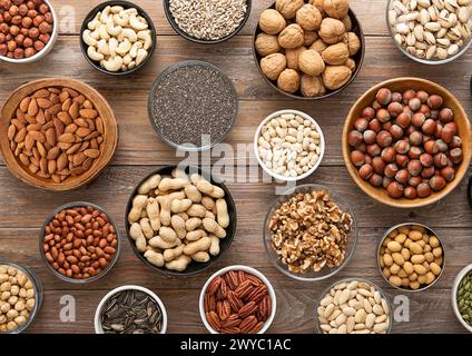 Erdnuss, Haselnuss, Walnuss, Mandeln, Pistazien, Sonnenblumen, Kürbis, Chia, Pekannuss und Cashew gemischte gesunde Nüsse und Samen in verschiedenen Schüsseln auf hölzernem Hintergrund. Stockfoto