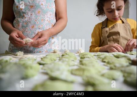 Selektiver Fokus auf hausgemachte Klößchen auf bemehlten Tischen vor dem Hintergrund der gemeinsamen Kochen von jungen Eltern und Tochter Stockfoto