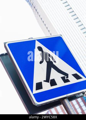 Ein Fußgängerschild steht deutlich vor einem klaren Himmel mit der Silhouette moderner Stadtarchitektur im Hintergrund. Das Zeichen indica Stockfoto