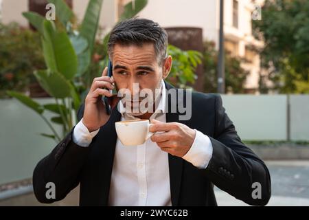 Porträt eines lächelnden Geschäftsmannes, der draußen mit einem Smartphone spricht. Stockfoto