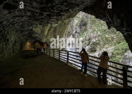 Touristen treffen sich entlang eines umzäunten Weges in einem Höhlentunnel und bewundern die atemberaubende Taroko-Schlucht draußen Stockfoto