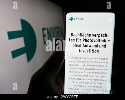 Person, die ein Mobiltelefon hält, mit Webseite der deutschen Solarfirma ENVIRIA Energy Holding GmbH vor dem Logo. Konzentrieren Sie sich auf die Mitte des Telefondisplays. Stockfoto