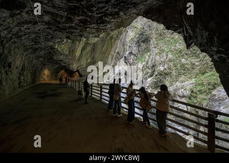 Touristen treffen sich entlang eines umzäunten Weges in einem Höhlentunnel und bewundern die atemberaubende Taroko-Schlucht draußen Stockfoto