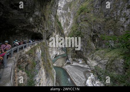 Touristen treffen sich entlang eines umzäunten Weges in einem Höhlentunnel und bewundern die atemberaubende Taroko-Schlucht draußen Stockfoto