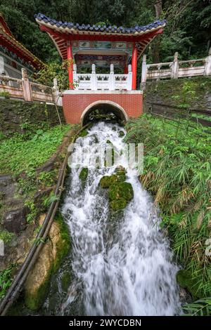 Eine malerische Struktur im Pagodenstil steht über einem schnell fließenden Bach in einer üppigen Umgebung und ist ein Beispiel für traditionelle asiatische Architektur Stockfoto