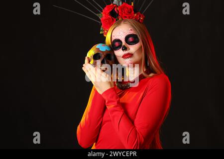 Junge Frau mit gemaltem Schädel auf schwarzem Hintergrund. Feier des mexikanischen Todestages (El Dia de Muertos) Stockfoto