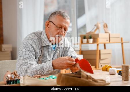 Reifer Schuhmacher repariert gebrochene Ferse am Tisch in der Werkstatt Stockfoto