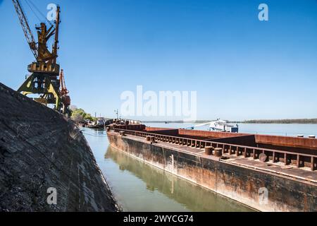 Binnenschiffsschiff und Industriekrane am Flusshafen an sonnigen Tagen Stockfoto