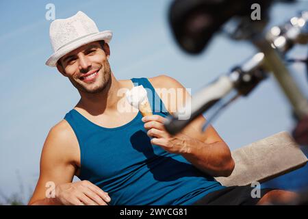 Mann, Eis und Porträt mit Fahrrad zum Entspannen im Freien, Reisen und Erholungspause im Sommerurlaub. Junge Person, lächle und sitze mit Stockfoto