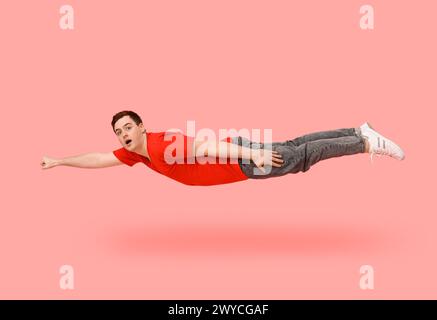 Überraschter junger Mann, der auf rosa Hintergrund fliegt Stockfoto