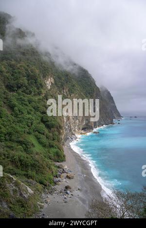 Majestätische Küste mit steilen Klippen und türkisfarbenen Meereswellen unter bewölktem Himmel Stockfoto