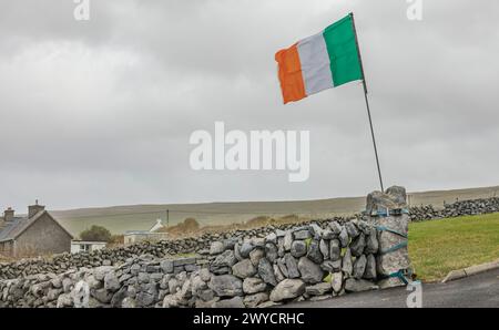 Irische Flagge, die im Wind flattert, an einem Torpfosten am Ende einer Steinmauer befestigt Stockfoto