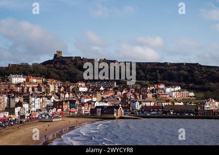 Eine Burgruine liegt hoch auf einem Hügel mit Blick auf einen Badeort mit Sandstrand in einer Bucht, Scarborough South Bay, North Yorkshire, England. Stockfoto