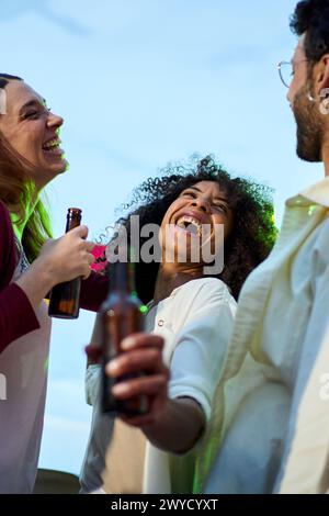Konzentrieren Sie sich auf die aufgeregte Afrikanerin, die eine Bierflasche mit lachenden Millennials-Freunden bei Sonnenuntergang hält Stockfoto