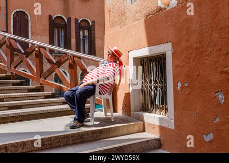 Ein Gondoliere in einem traditionellen rot-weißen Hemd sitzt in einem Stuhl, der von Ponte Vinanti in Dorsoduro und Santa Croce, Venedig, Italien, schläft Stockfoto