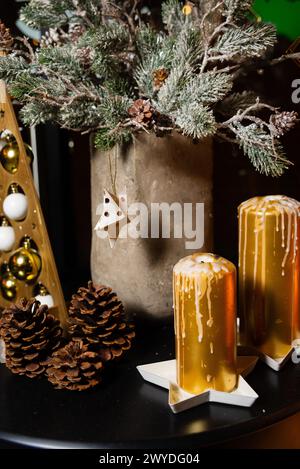 Eine gemütliche Weihnachtskulisse mit satinierten Tannenzweigen, tropfenden Kerzen und Tannenzapfen auf dunklem Hintergrund. Stockfoto