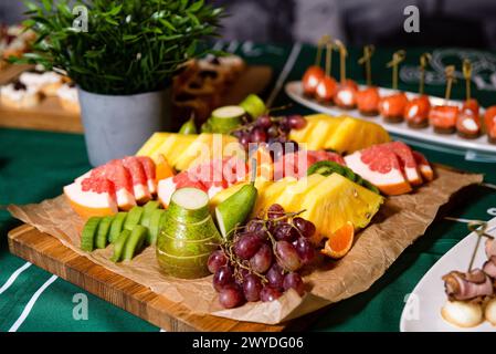 Eine herrliche Auswahl an frischen Obstscheiben, einschließlich Ananas, Wassermelone und Trauben, die ordentlich auf einem Holzbrett präsentiert werden. Stockfoto