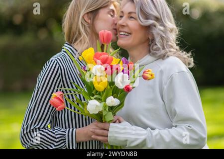 Tochter umarmt Mutter, konzentriert sich auf Tulpenstrauß. Stockfoto