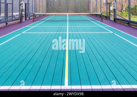 Elevated Platform Tennis, Paddle Ball Courts mit gelben Pickelballlinien, Netz und Hühnerdrahtzaun. Die Bodenfläche ist grün, kastanienbraun, weiß und Stockfoto