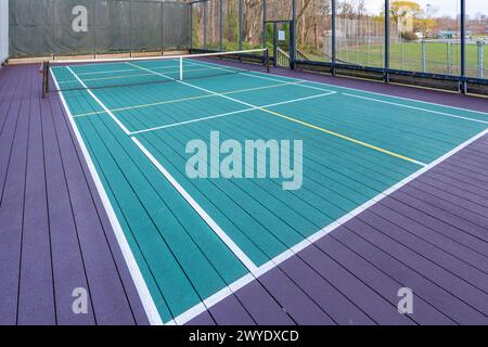 Elevated Platform Tennis, Paddle Ball Courts mit gelben Pickelballlinien, Netz und Hühnerdrahtzaun. Die Bodenfläche ist grün, kastanienbraun, weiß und Stockfoto