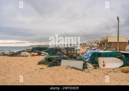 Angelausrüstung und Boote verstreut an einem Sandstrand unter bewölktem Himmel. Stockfoto