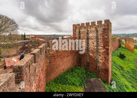 Die robusten roten Mauern von Silves Castle, mit einem Besucher, der die Aussicht von der Stadtmauer genießt. Stockfoto