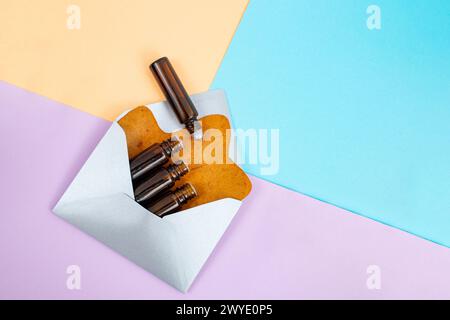 Viele Flaschen ätherischer Öle und Rollen in einem silbernen Umschlag mit einem getrockneten Baumblatt auf angeordnetem farbenfrohen Hintergrund, abstrakte alternative Medizin zurück Stockfoto