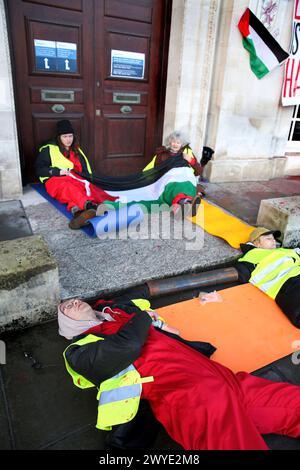 Palästinensische aktionäre sitzen in Zweiergruppen bei einer Demonstration vor dem Rathaus des Bezirks Somersetís. Unterstützer der Palästinensischen Aktion blockieren den Eingang zur County Hall mit Sperren und sprühen rote Farbe auf das Äußere des Gebäudes. Die Demonstranten fordern, dass der Stadtrat von Somerset den Mietvertrag für Büroflächen beendet, die sie an Elbit Systems in Aztec West, Bristol, vermieteten. Sie argumentieren, dass die von Elbit Systems in Großbritannien hergestellten Waffen von der israelischen Verteidigungsstreitkräfte gegen Palästinenser in Gaza und anderswo eingesetzt werden. Bei den israelischen Bombenanschlägen im Gazastreifen sind seit Oktober 2023 mehr als 30.000 Palästinenser ums Leben gekommen. Blass Stockfoto